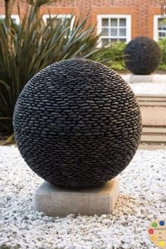 a large black ball sitting on top of a white stone slab in front of a building