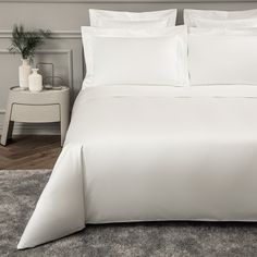 a bed with white sheets and pillows on top of carpeted floor next to nightstands