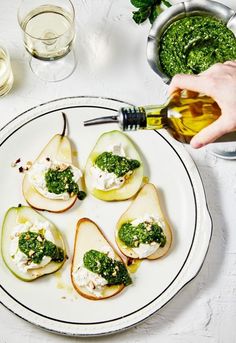 a white plate topped with pears covered in cheese and pesto next to glasses of water