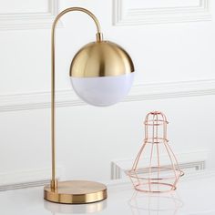 a white and gold lamp on a table next to a wire holder with a light bulb