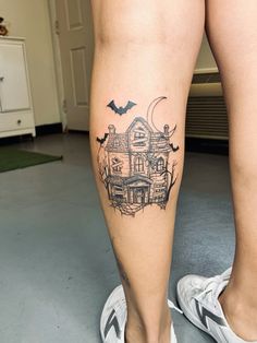 a woman's leg with a house and bats tattoo on her left side calf