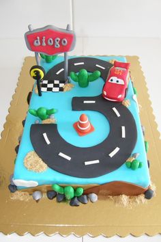 a birthday cake that is shaped like a race track with cars on it and a street sign