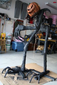 a sculpture of a spider holding a pumpkin on top of a piece of cardboard in a garage