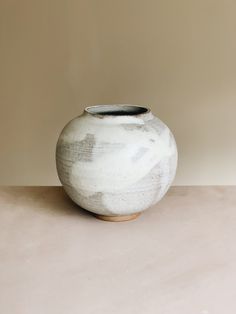 a white vase sitting on top of a table next to a brown and beige wall