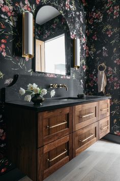 a bathroom with floral wallpaper and wooden vanity, two mirrors on the wall above it