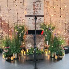 an arrangement of flowers and candles on a stand in front of a brick wall with string lights