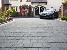 a car is parked in front of a house with two people walking by the driveway