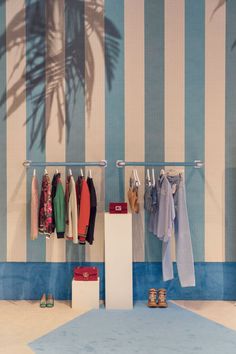 a clothing rack with clothes hanging on it in front of a blue and white striped wall