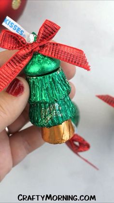 a hand holding a green christmas tree ornament with a red ribbon on it