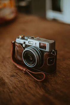 a camera sitting on top of a wooden table next to a brown leather case and strap