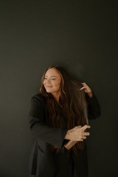 a woman standing in front of a black wall with her hair blowing back and holding an umbrella