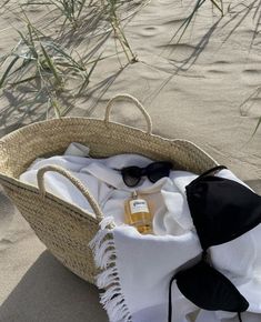 an open wicker basket on the beach with clothing and sunglasses