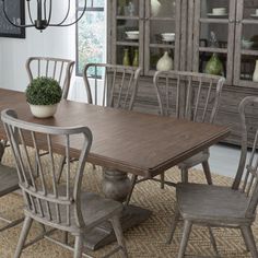 a dining room table with chairs and a vase on it's centerpiece in front of a china cabinet