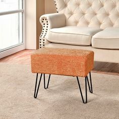 an orange ottoman sitting on top of a rug in front of a white couch and window