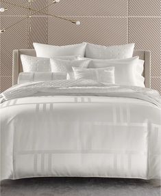 a bed with white sheets and pillows on top of it in a room that has beige walls