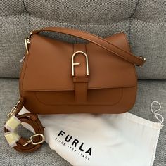 Nwt Furla Flow Top Handle M Bag (Medium Size Of The Range). It Can Be Carried By Hand Or With The Log Strap. Purchased Directly From Furla And A New Edition, But I’m Cleaning Out My Bag Collection. Interior Details 1 Flat Open Pocket Exterior Details Fula Logo/Single Handle/Open Pocket On The Back Material Claris Lux Calf Leather Strap Information Removable/Adjustable Leather Strap Strap Length Max 42.52 In Strap Length Min 37.6 In Closure Magnet Closure Hardware Furla Arch Gasket Product Code W Elegant Saddle Bag With Branded Hardware For Daily Use, Cognac Satchel Bag With Branded Hardware, Flap Shoulder Bag With Branded Hardware For Shopping, Daily Use Flap Bag With Branded Hardware, Chic Flap Bags With Branded Hardware, Chic Flap Bag With Branded Hardware, Elegant Flap Satchel, Modern Cognac Shoulder Bag With Branded Hardware, Flap Bags With Branded Hardware