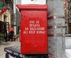 a red box sitting on the side of a street next to a pole with writing on it