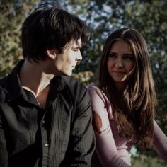 a young man and woman sitting next to each other in the park, looking at each other