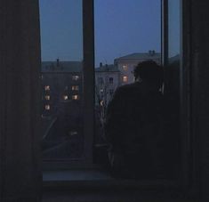 a man sitting in front of a window looking out at the night sky and buildings