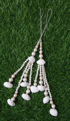 some white seashells and pearls hanging from a string on green grass in the sun