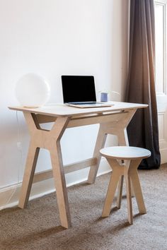 a laptop computer sitting on top of a wooden desk next to a white chair in front of a window