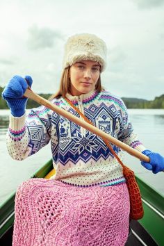 a woman in a knitted sweater and hat rowing a boat on the water with a paddle