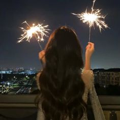 a woman holding two sparklers in her hand and looking out over the city at night