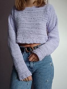 a woman with her hands in her pockets wearing a purple knitted sweater and jeans