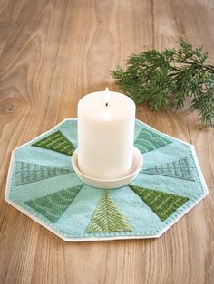 a white candle sitting on top of a wooden table next to a green napkin and pine branch