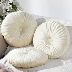 three round pillows sitting on top of a bed next to a potted plant and pillow