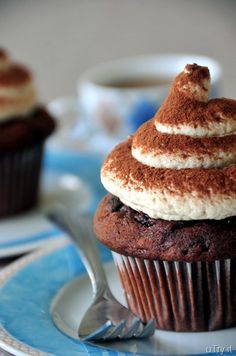 a chocolate cupcake with white frosting on a blue and white plate next to a silver spoon