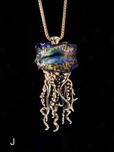 "This dramatic Portuguese Man of War Jelly Fish Pendant wears a crown of dichroic glass. The coiled and flowing tentacles are cast in sterling sliver and the overall length of the pendant is 2-3/8\" (60 mm) long. This is Alisha's second and most complex design collaboration with glass artist John Rizzie who has created a rainbow of dichroic glass crests from which Alisha's coiled sterling silver tentacles descend. Each dichroic glass jelly fish crest is unique so choose from a rainbow of colors. Whimsical Silver Glass Jewelry, Ocean-inspired Silver Glass Necklace, Ocean-inspired Silver Glass Jewelry, Jellyfish Tentacles, Jellyfish Necklace, Magic Charms, Complex Design, Jewelry Ocean, Sea Jewelry