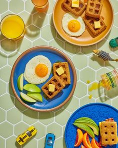 two plates with waffles, eggs and fruit on them next to orange juice