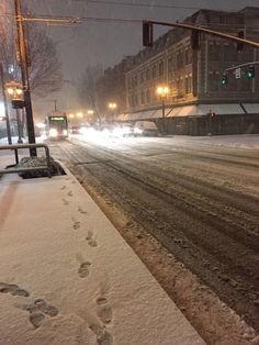 a snowy street with tracks in the snow next to traffic lights and cars driving down it