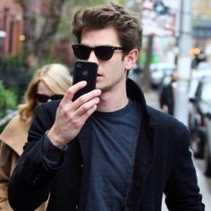 a man in sunglasses is looking at his cell phone while walking down the street with other people