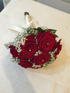 a bouquet of red roses and baby's breath on a table with white ribbon