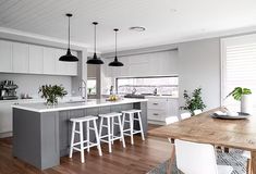 a kitchen with white cabinets and gray island in the center is surrounded by bar stools