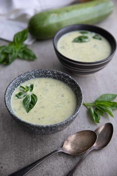 two bowls filled with soup on top of a table next to cucumbers and spoons