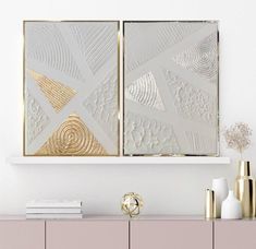 two white and gold framed art pieces on a wall above a dresser with vases