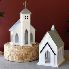 two small white houses sitting next to each other on top of a basket near a christmas tree