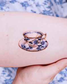 a woman's arm with blue and white designs on it holding a coffee cup