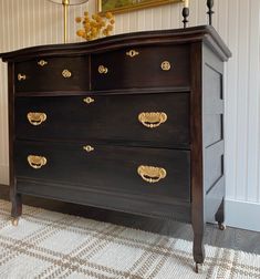 a black dresser with gold knobs in a living room next to a painting on the wall