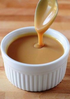 a spoon is pouring caramel sauce into a small white bowl on a wooden table