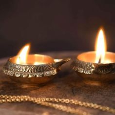 two gold tea lights sitting on top of a wooden table next to a golden chain