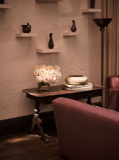 a table with flowers and vases on it in front of a wall mounted shelf