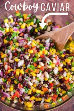 a glass bowl filled with black beans, corn and cilantros next to a wooden spoon