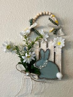 a white wall hanging with flowers and a wooden bunny decoration on it's side