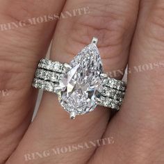 a woman's hand holding a ring with a pear shaped diamond on it and two rows of diamonds around the band