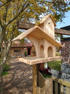 a wooden bird house sitting on top of a wooden fence next to a small tree