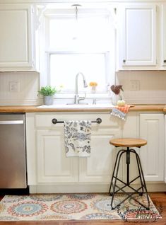 a kitchen with white cabinets and an area rug in front of the sink that has a wooden stool on it